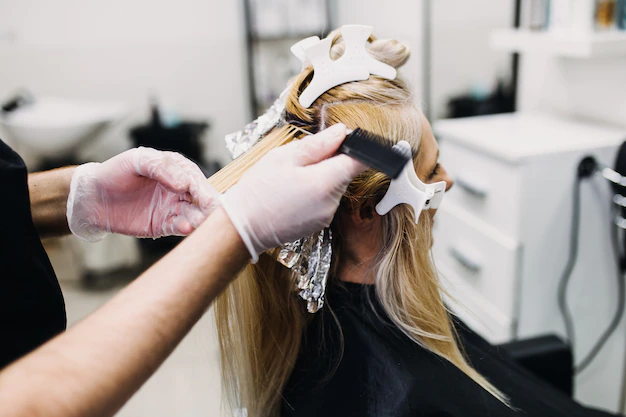 o cabeleireiro esta tingindo o cabelo feminino fazendo mechas de cabelo para sua cliente com um papel aluminio 473712 884